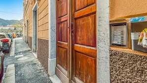 Une vue de rue avec une porte à deux battants en bois, des voitures garées et un bâtiment doté d’un mur à la texture particulière.