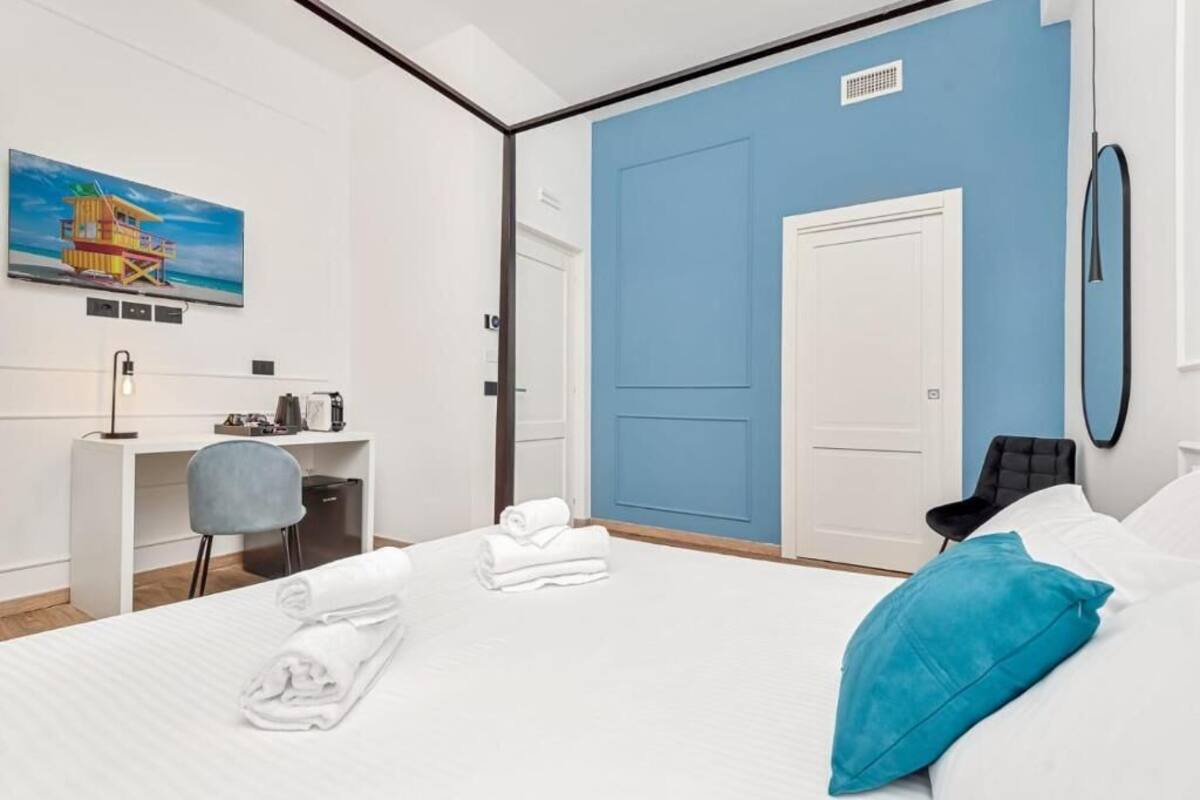 Een hotelkamer met een bed, een bureau, een stoel, een blauwe muur en een schilderij van een redershut.