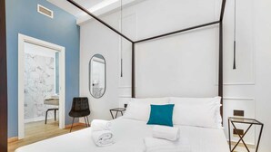 Une chambre d’hôtel moderne avec un lit à baldaquin, une petite table, une chaise et un miroir.