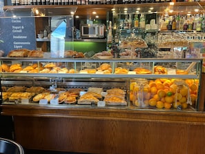 Un expositor de pastelería con diversos productos de repostería y una variedad de bebidas embotelladas.