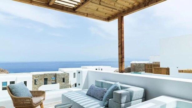 Un espacio moderno para sentarse al aire libre con vistas al mar, que incluye un sofá, una silla de mimbre y un jacuzzi.