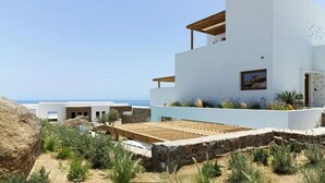 Un edificio moderno y blanco con una terraza de madera, rodeado de follaje y vistas al mar.