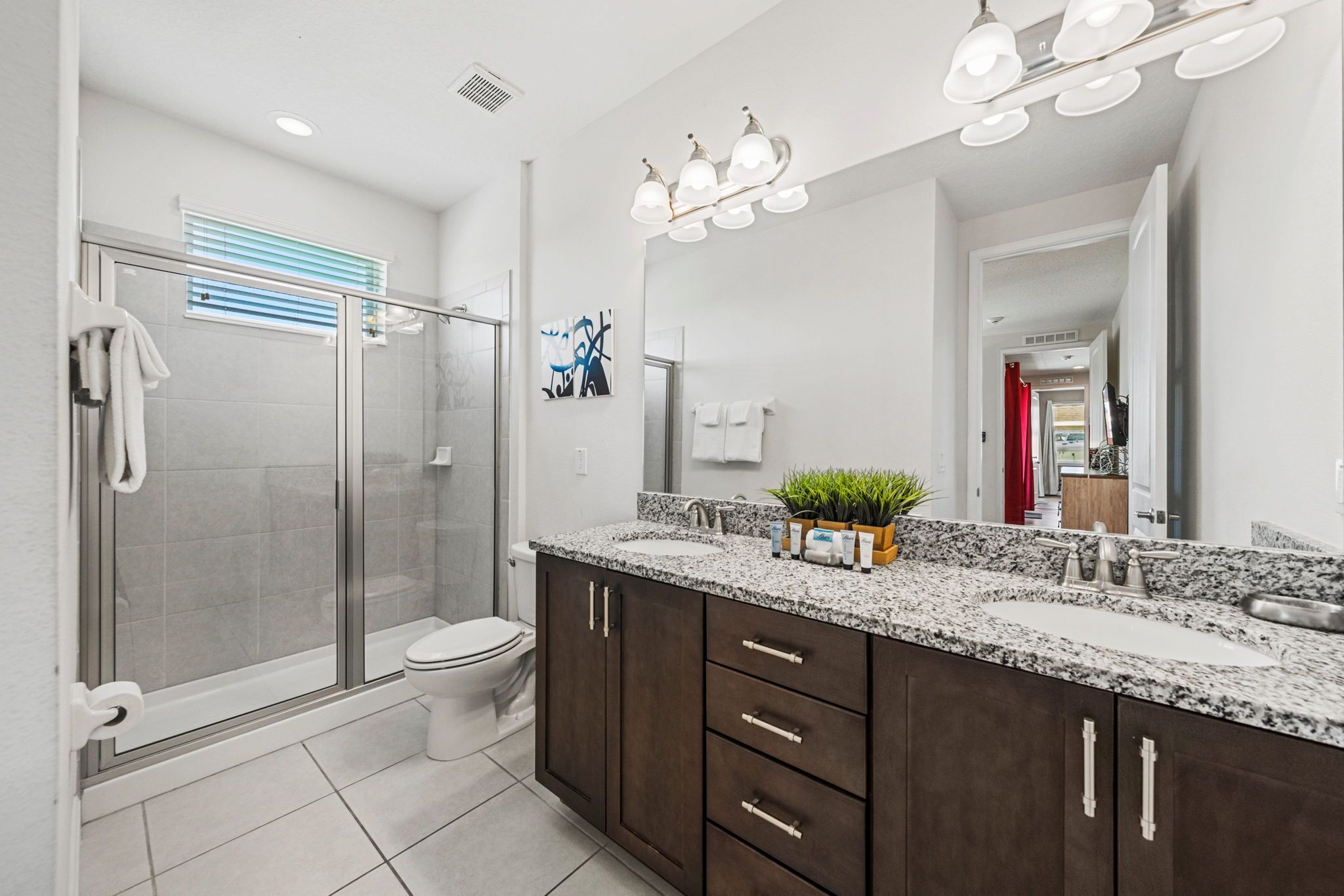 A modern bathroom with a glass shower enclosure, a toilet, a sink with a granite countertop, and dark wooden cabinets.