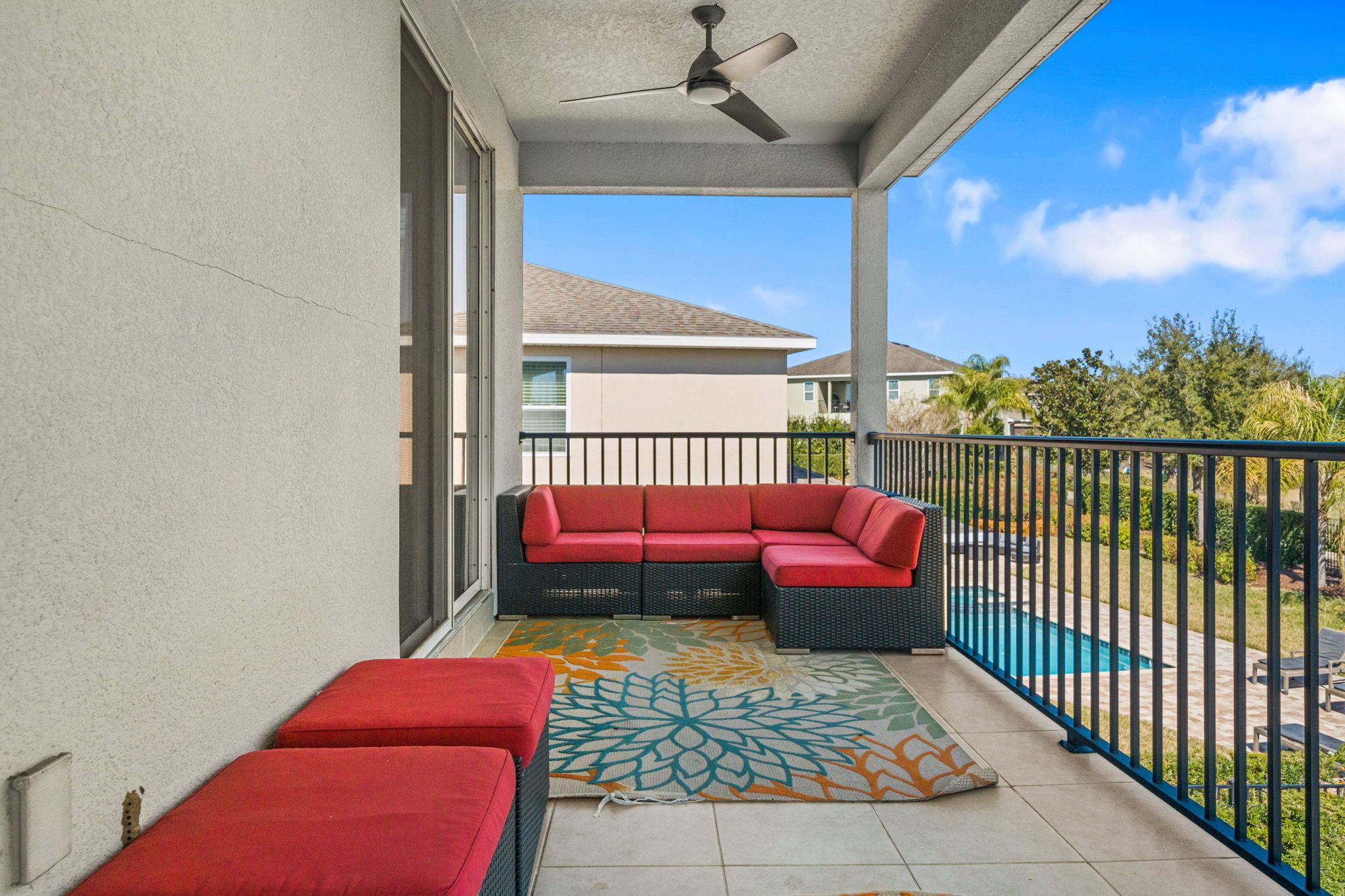 A balcony with a red sectional sofa, a small table, and a ceiling fan.