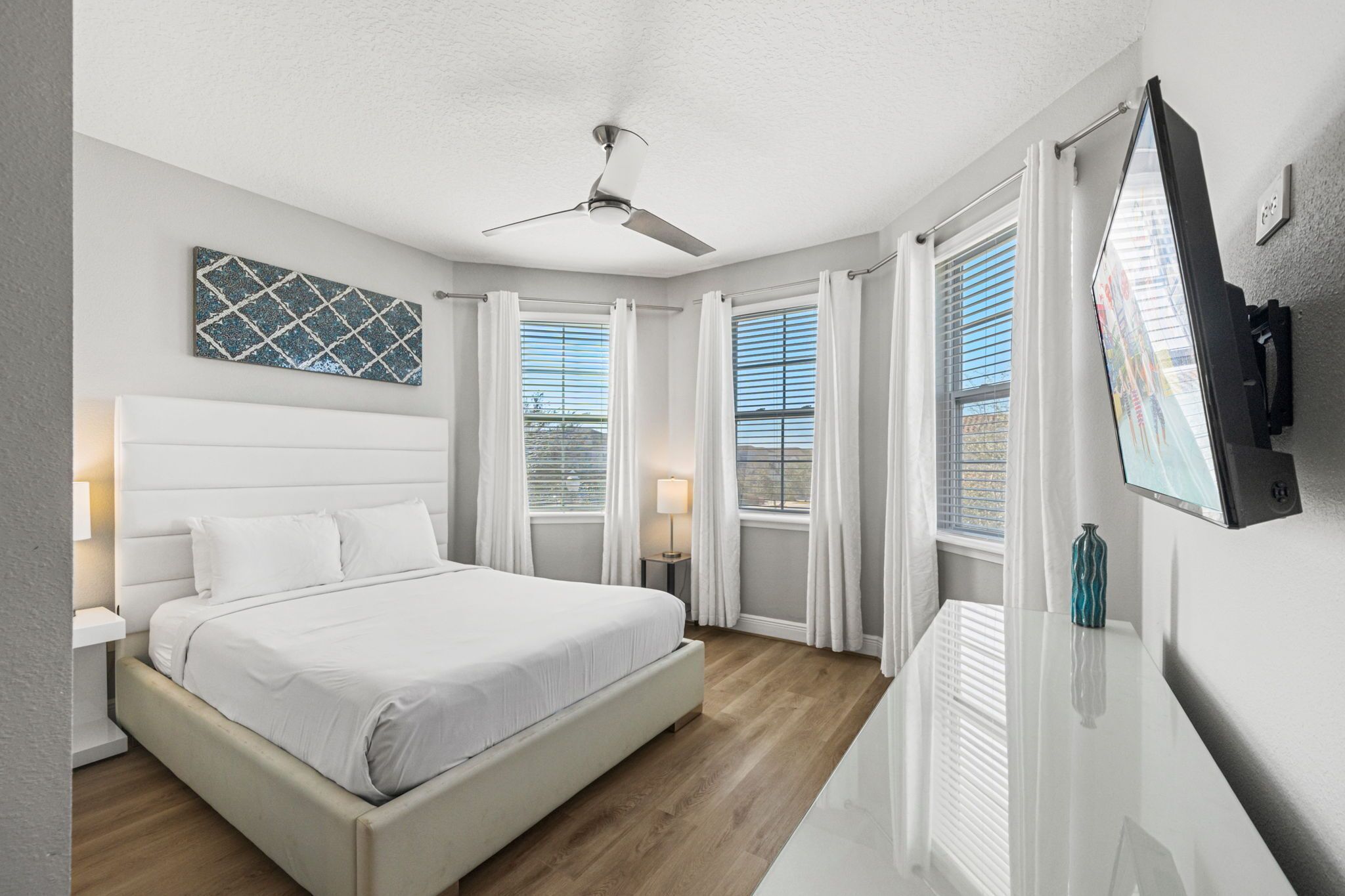 A modern bedroom with a large bed, ceiling fan, and a TV mounted on the wall.