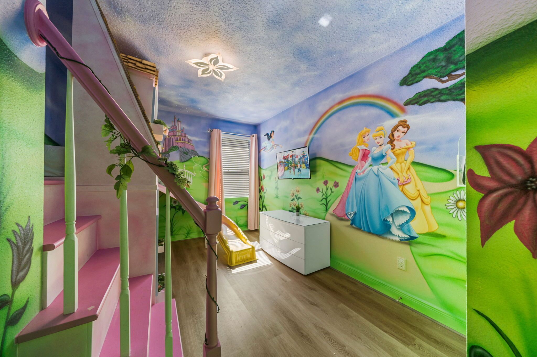 A room with a staircase, a white console table, and a mural of Disney princesses.