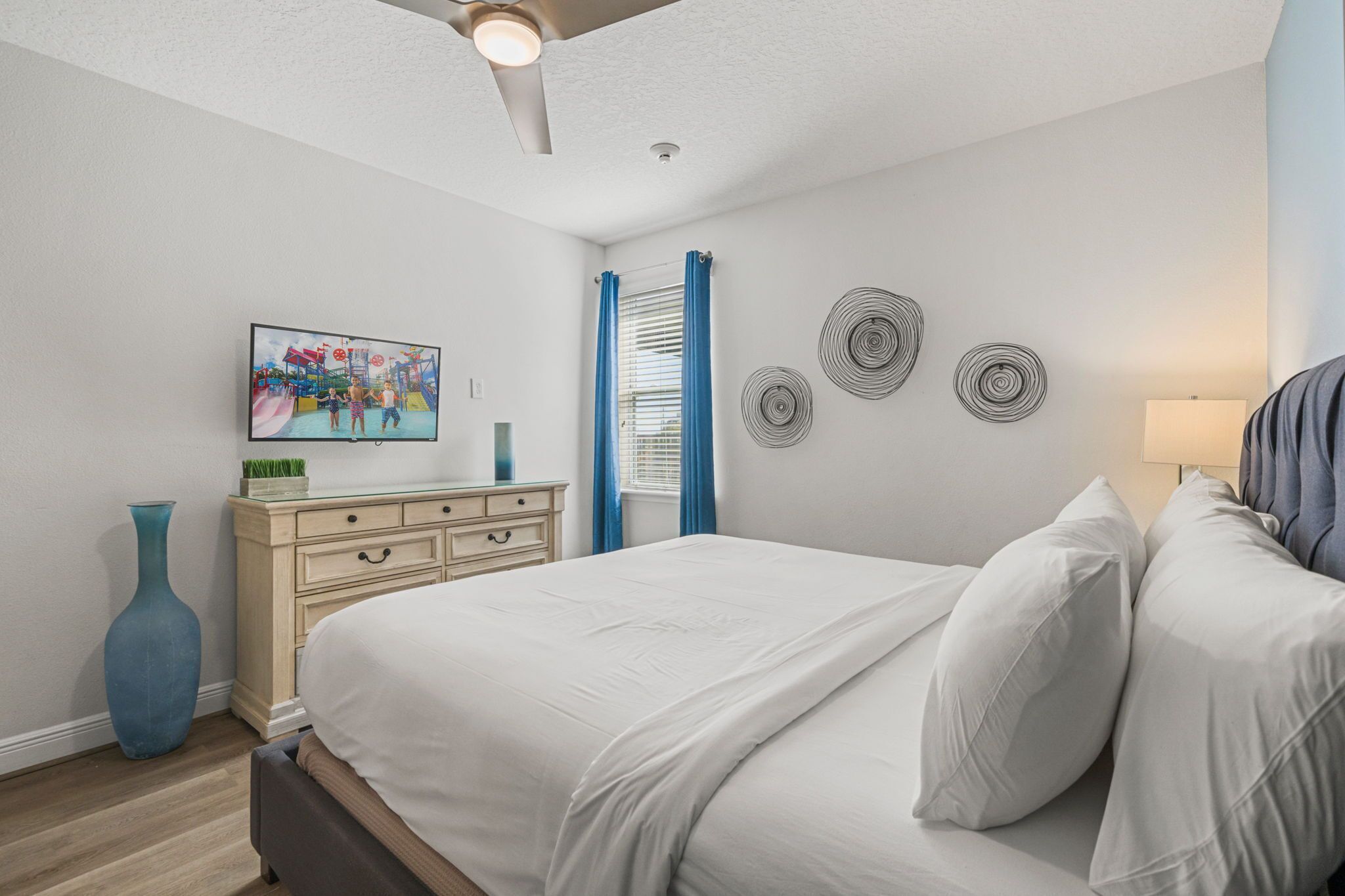 Een slaapkamer met een bed, dressoir, televisie, kunstwerken en wanddecoratie.