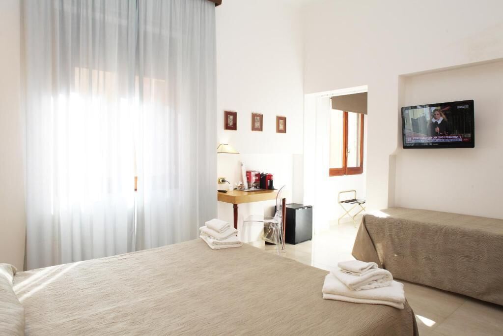 A hotel room with a bed, a desk with a lamp, a TV, and a window with curtains.