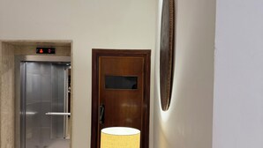 Ein Korridor mit einer Holztür, einer Wandleuchte und einem Aufzug.