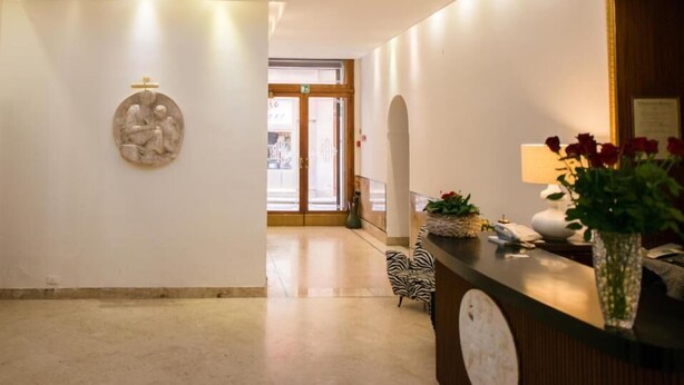Eine Hotelhalle mit Oberlicht, einer Rezeption, einer Wandskulptur und einem Zebra-Stuhl.