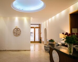 Et hotellobby med ovenlys, en receptionsdisk, en vægmonteret skulptur og en stol med zebrastriber.