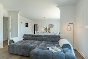 Un salon moderne avec un canapé d’angle, un coin repas à l’arrière-plan et une lampe sur pied.