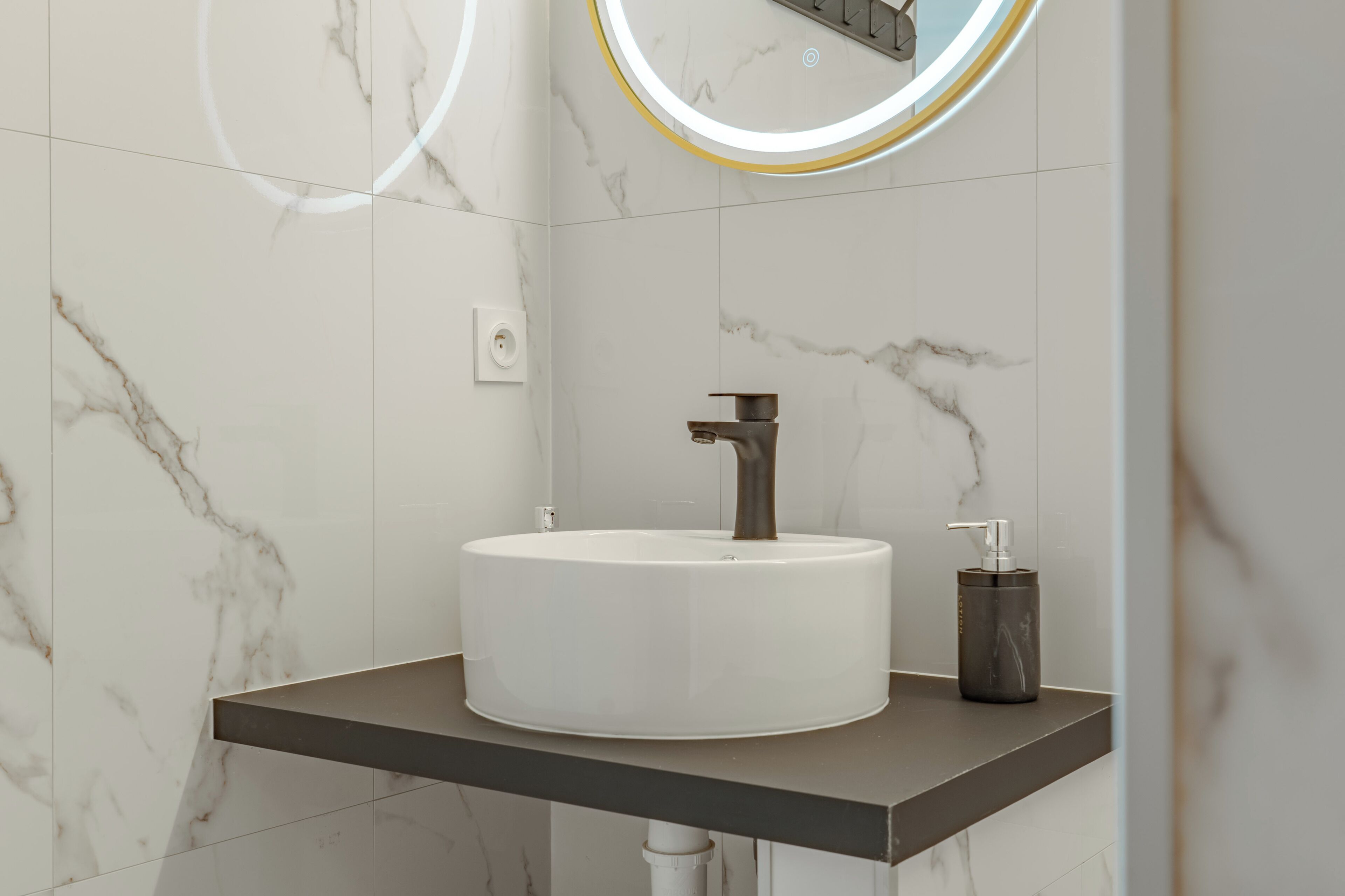 A bathroom with a white marble sink, a modern faucet, and a soap dispenser on a dark countertop.