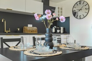 A modern kitchen with a black countertop, a vase with pink flowers, and a wall clock.