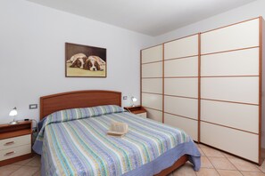 A bedroom with a bed, a nightstand, a bedside table, a lamp, a picture on the wall, and a sliding closet door. - Casa delle Vigne by Wonderful Italy (Olbia)
