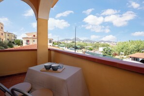 Un balcon avec une table dressée pour deux personnes, offrant une vue sur le paysage urbain, avec ses bâtiments et ses montagnes.