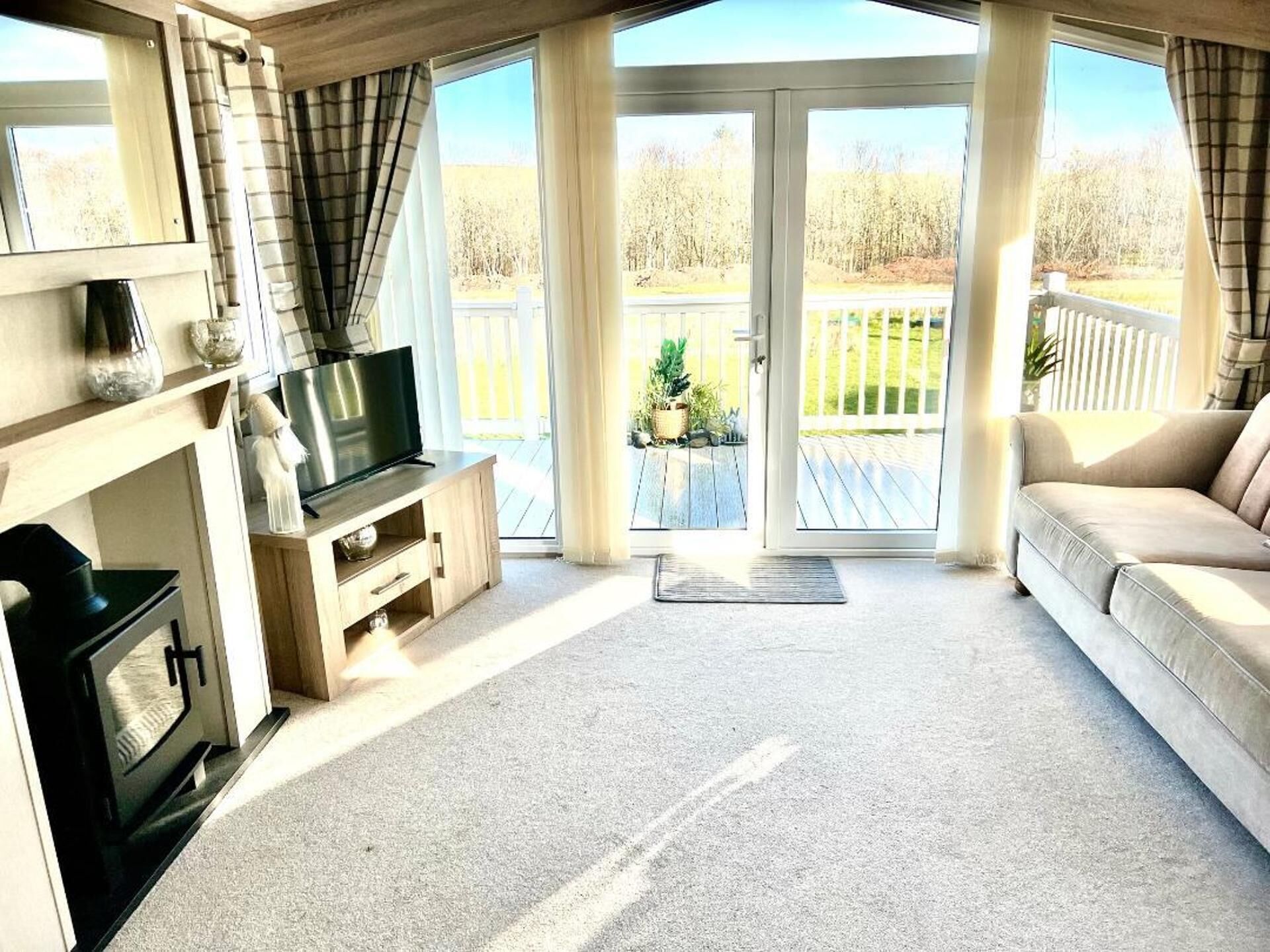 Sala de estar con chimenea, televisor y sofá, que da a una terraza con vistas a árboles.