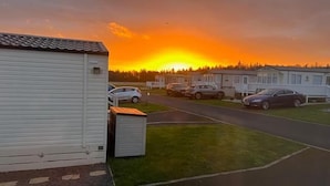 A row of mobile homes with a parking area in front, under a sunset sky. - Holiday Cabin Sleeps 5, Pets, Edinburgh Festival (Dunbar)