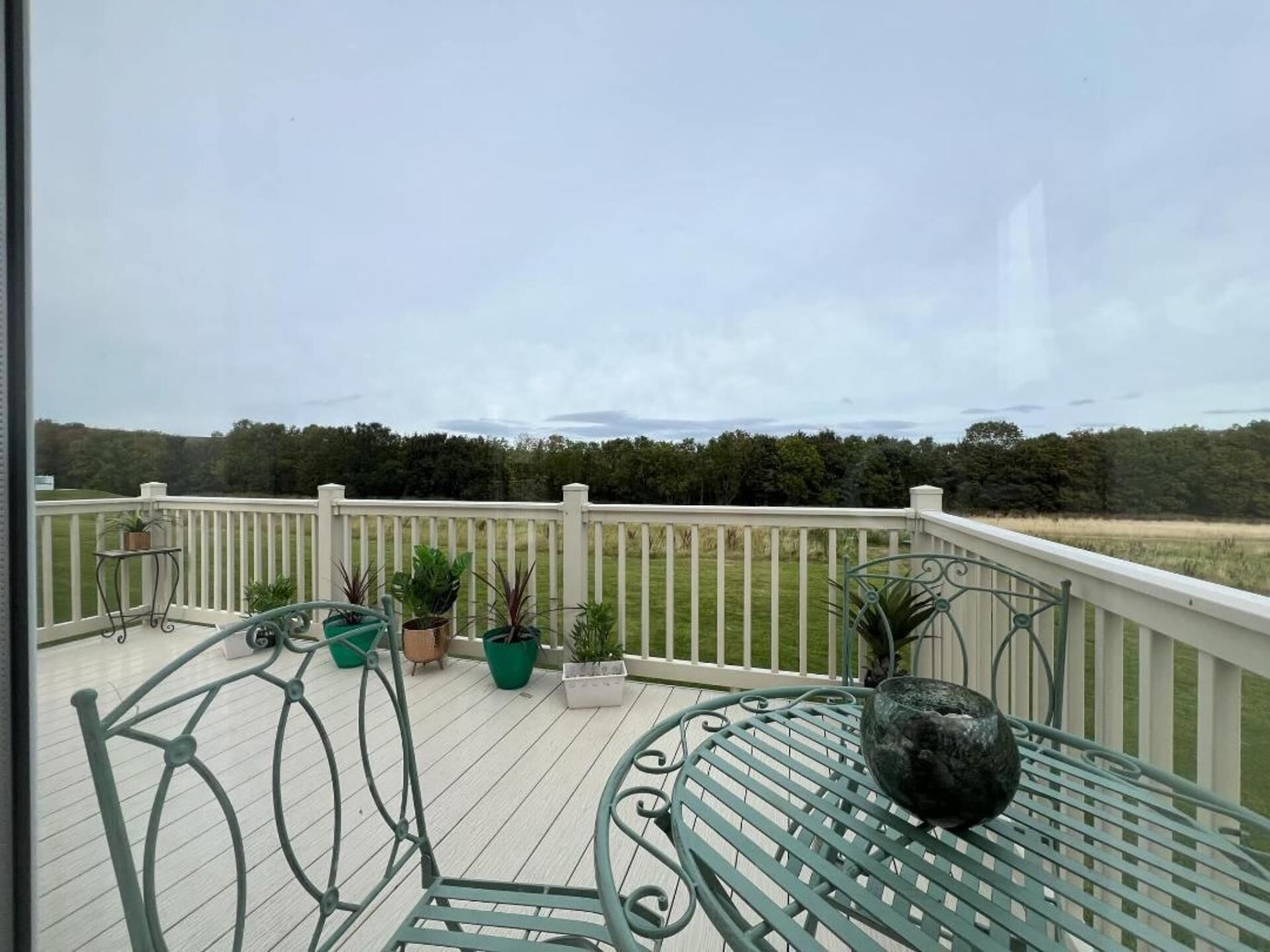 A balcony with a white railing, green metal chairs, and potted plants.