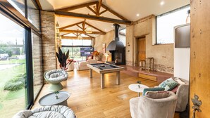 Amplia sala de estar con mesa de billar, asientos cómodos, chimenea y ventanas grandes que ofrecen vistas al exterior.