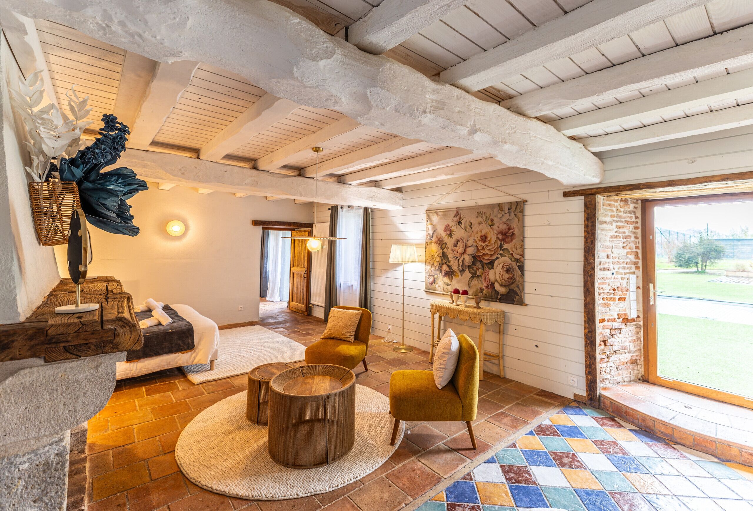 Una stanza accogliente con soffitto in legno, un'ampia finestra, un tavolo rotondo in legno e una poltrona gialla.