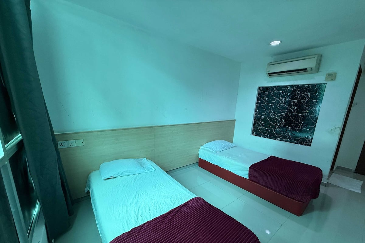A room with two beds, a wall-mounted air conditioner, and a large window with a cracked view.