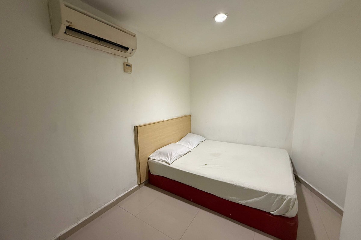 A small, single-bed room with a wooden headboard, white bedding, and a ceiling-mounted air conditioning unit.