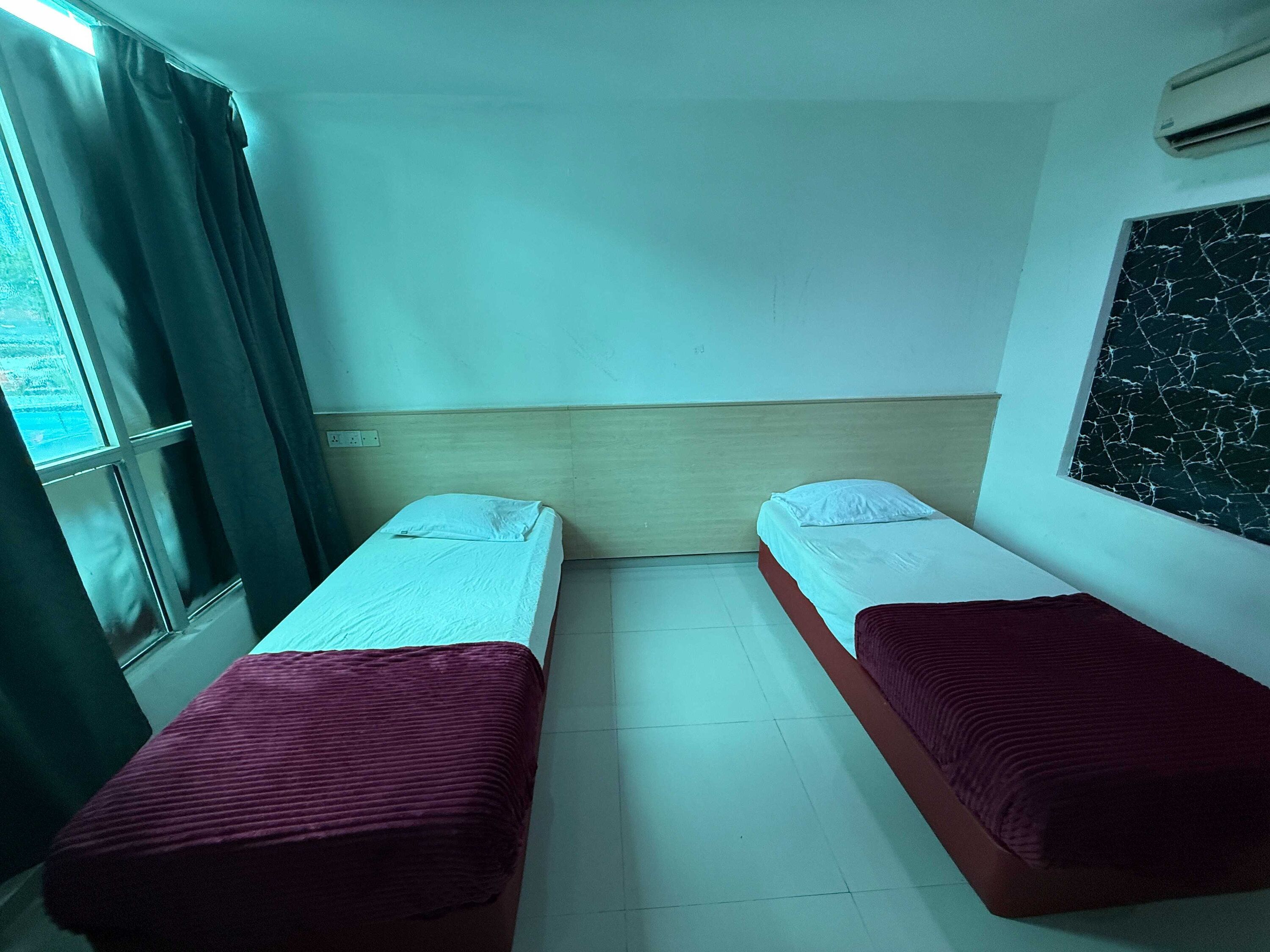 A room with two beds, a window with curtains, a wall-mounted air conditioner, and a marble-patterned wall.