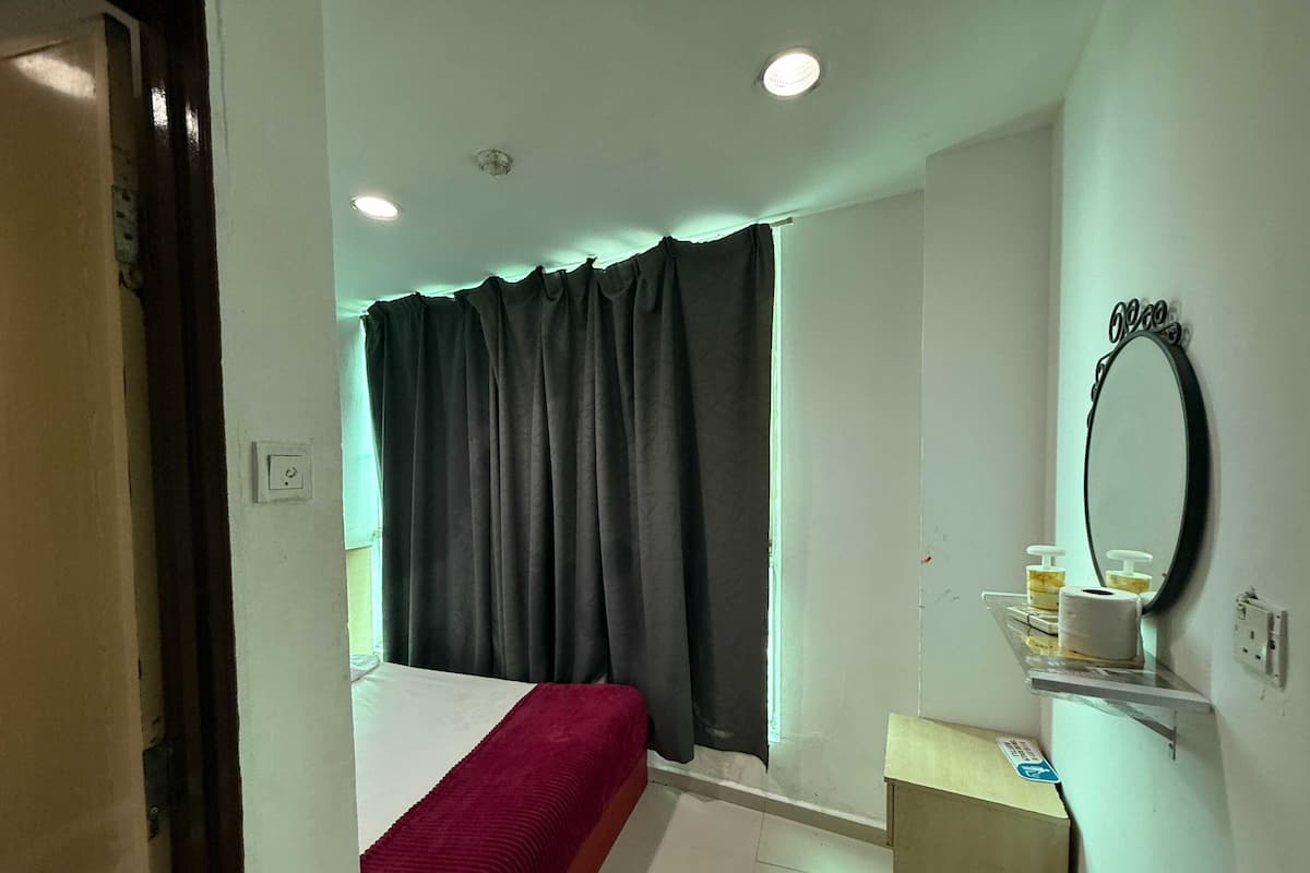 A hotel room with a bed, a window with curtains, a mirror, and a small table with toiletries.