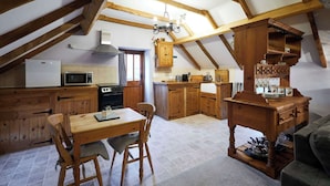 A rustic kitchen with wooden beams, a dining table, chairs, a refrigerator, a microwave, an oven, and a chandelier. - Host & Stay | The Grainary (Bridlington)