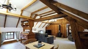 A rustic interior with exposed wooden beams, a dining area with a table and chairs, a sofa, a fireplace, and a television. - Host & Stay | The Grainary (Bridlington)