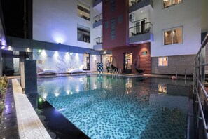 Ein Schwimmbad mit Fliesenboden, umgeben von einem Gebäude mit Balkonen und Fenstern.