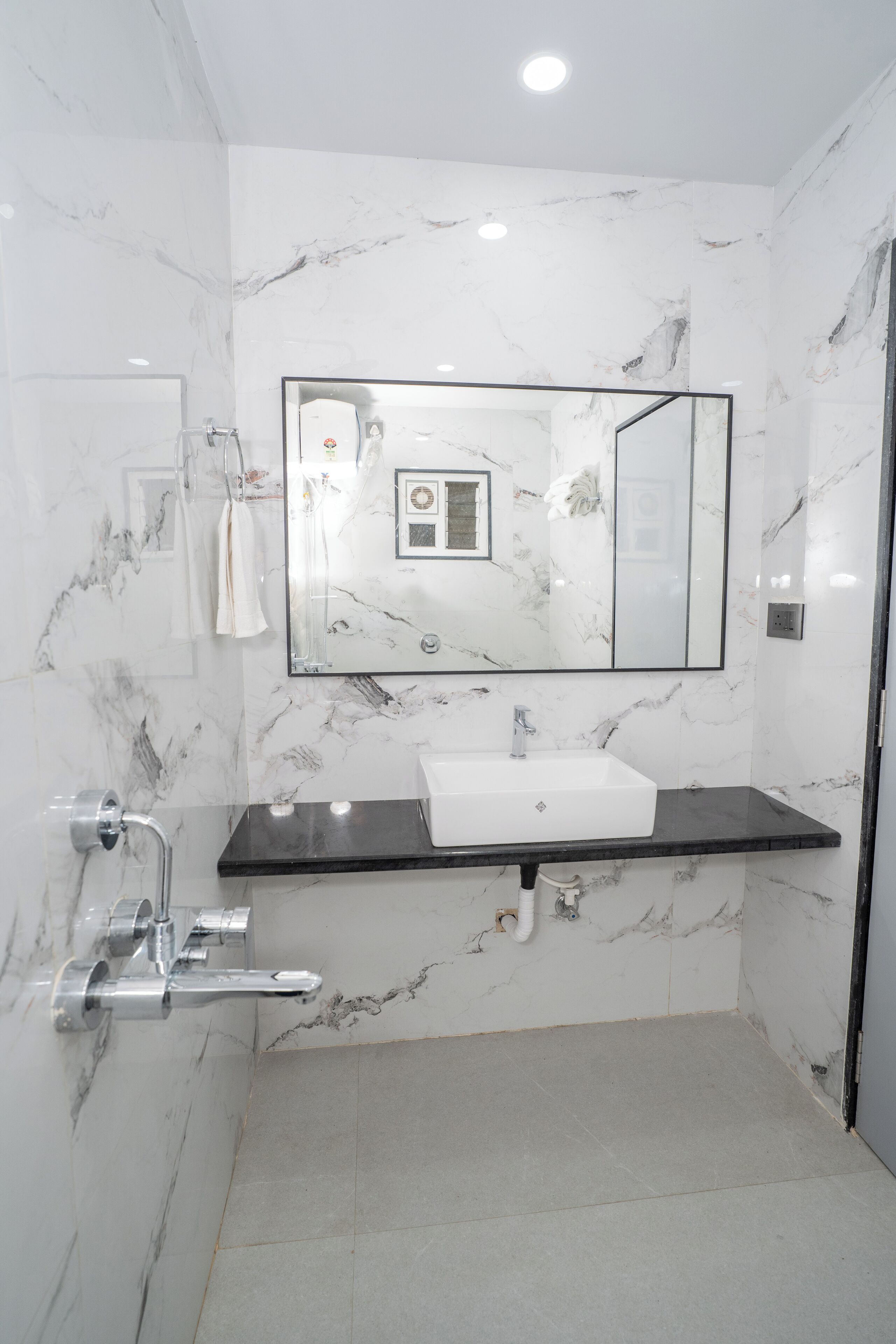Un baño con lavamanos de mármol blanco, encimera negra y un espejo grande.