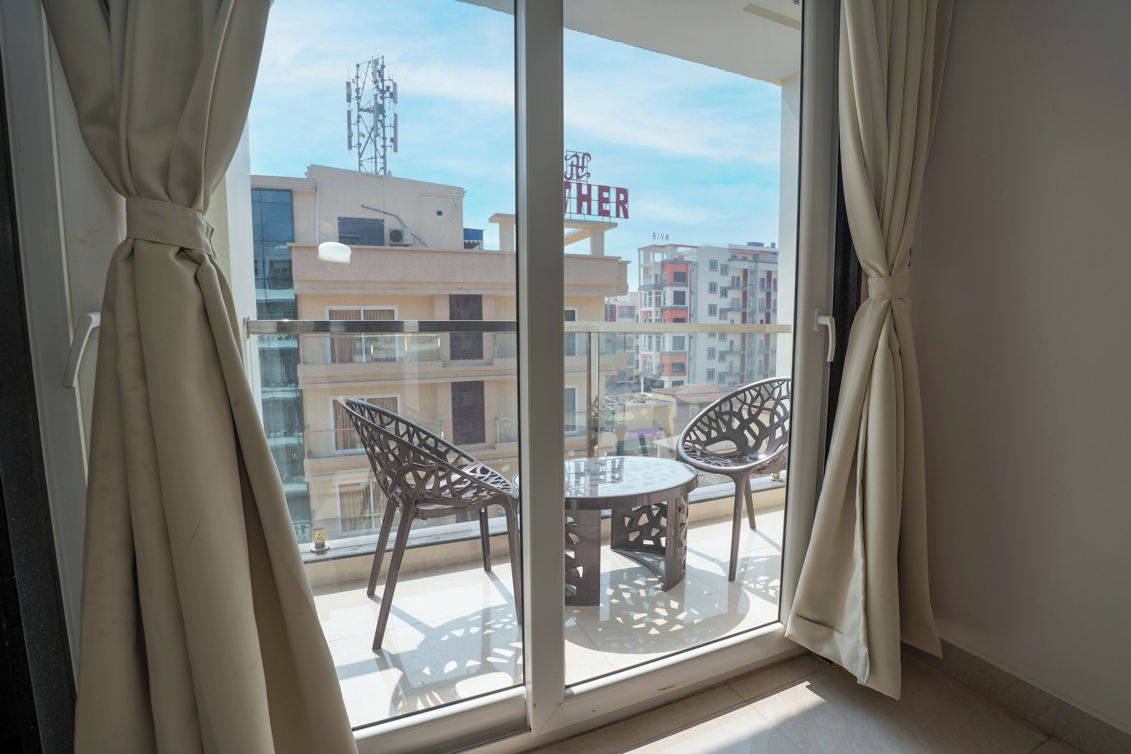 A balcony with two chairs and a table, a glass door, and a view of buildings in the background.