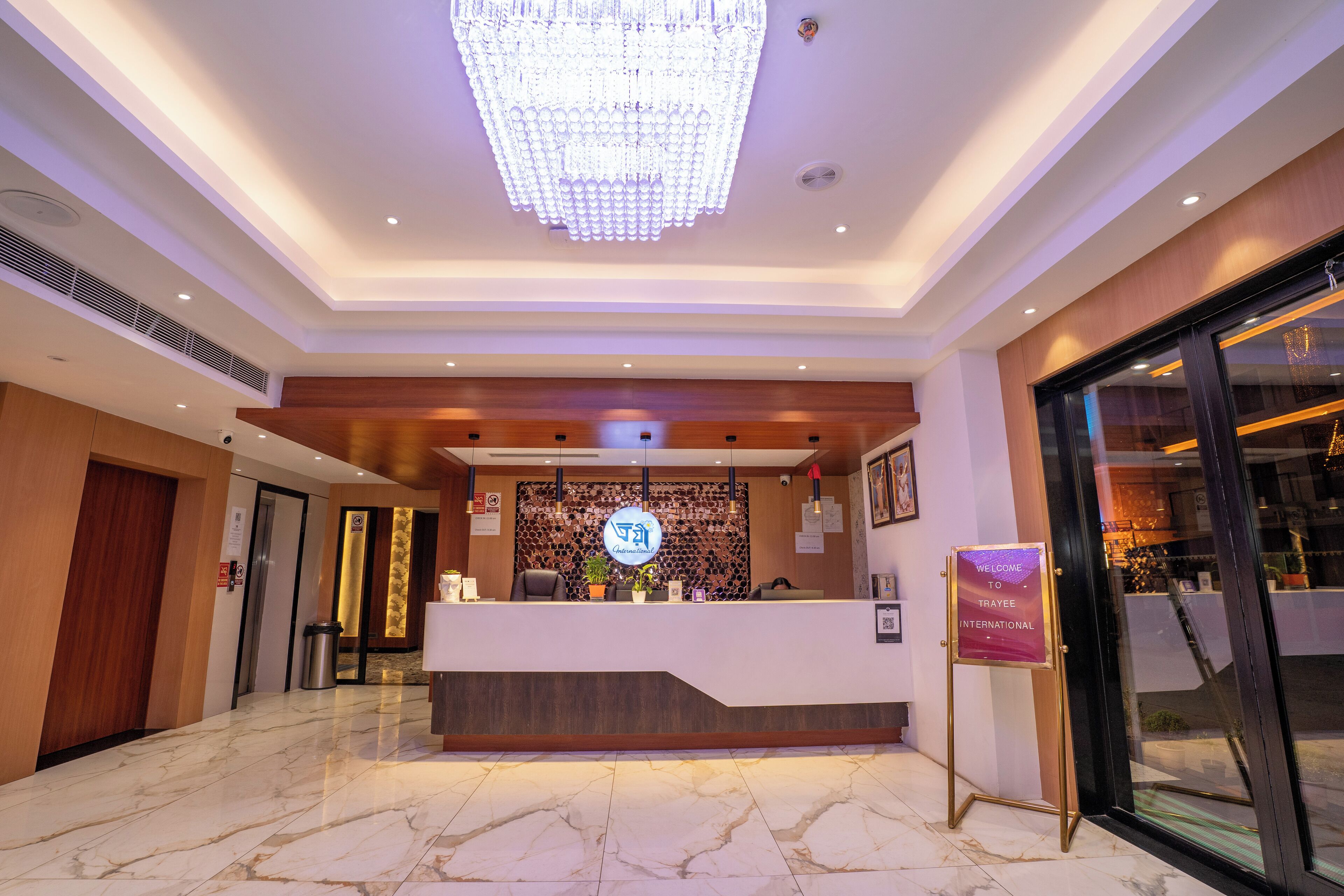 Un hall d'accueil d'hôtel agrémenté d'un lustre moderne, d'un comptoir de réception et d'une enseigne accueillant les clients à l'hôtel Traye International.