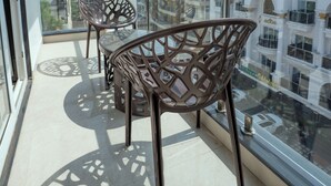 Een balkon met twee rieten stoelen en een tafeltje, met uitzicht op een stadsbeeld met witte gebouwen en een heldere lucht.