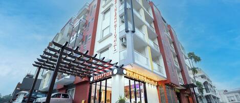 A multi-story hotel with a reception area, outdoor seating, and a parking lot.