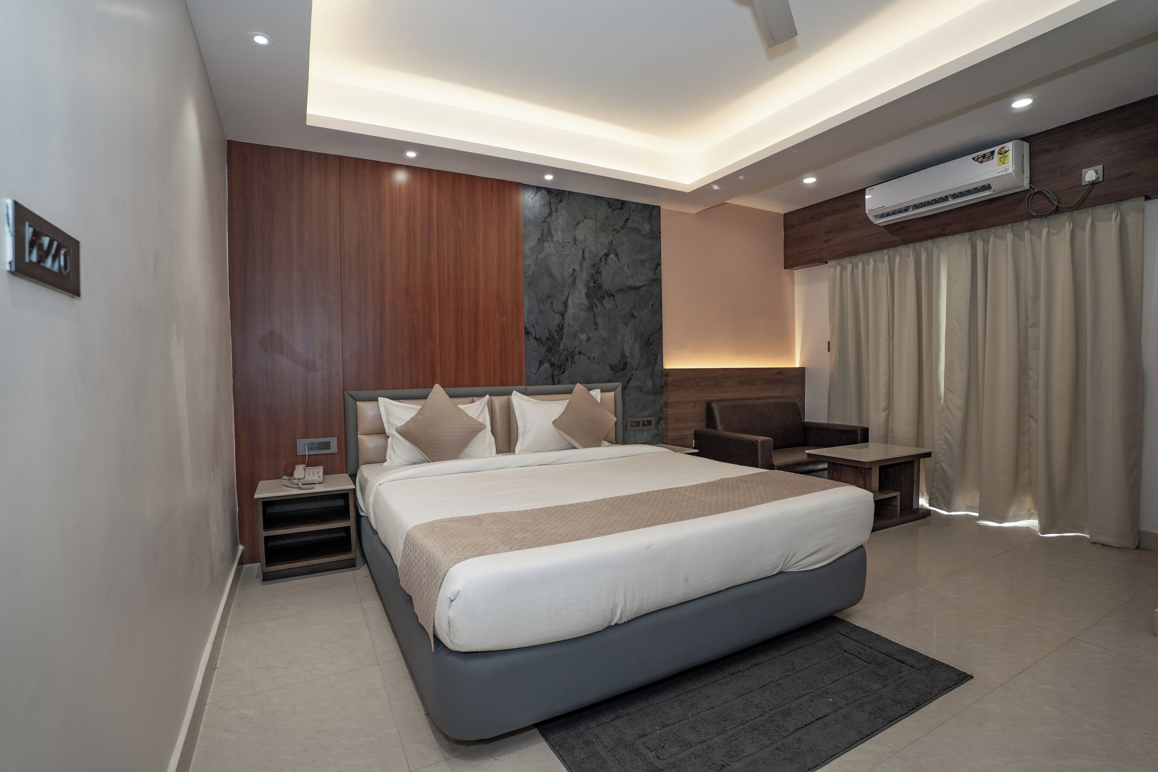 Una habitación de hotel moderna con una cama grande, paneles de madera, una pared de acento de mármol, un equipo de aire acondicionado y vistas al exterior.