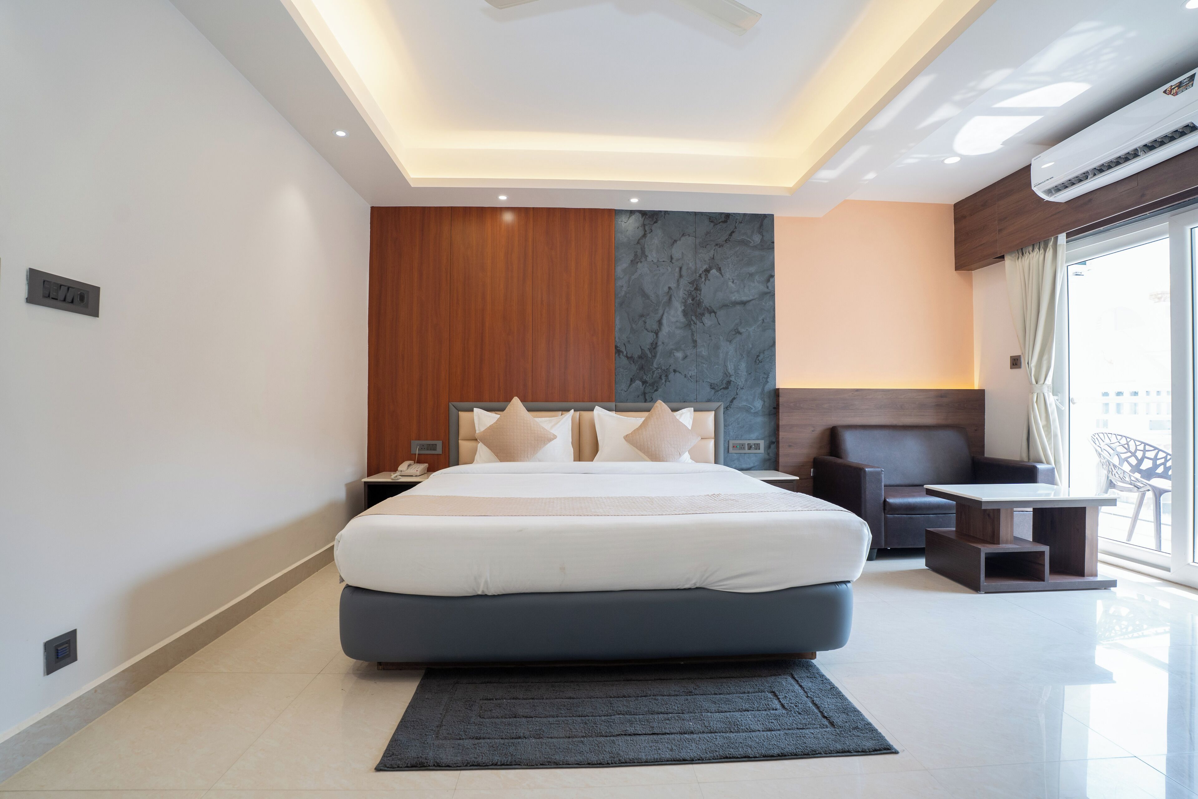 Een moderne hotelkamer met een groot bed, een houten accentmuur, een marmeren gedeelte, een donkere bank, een kleine tafel en een groot raam met uitzicht.
