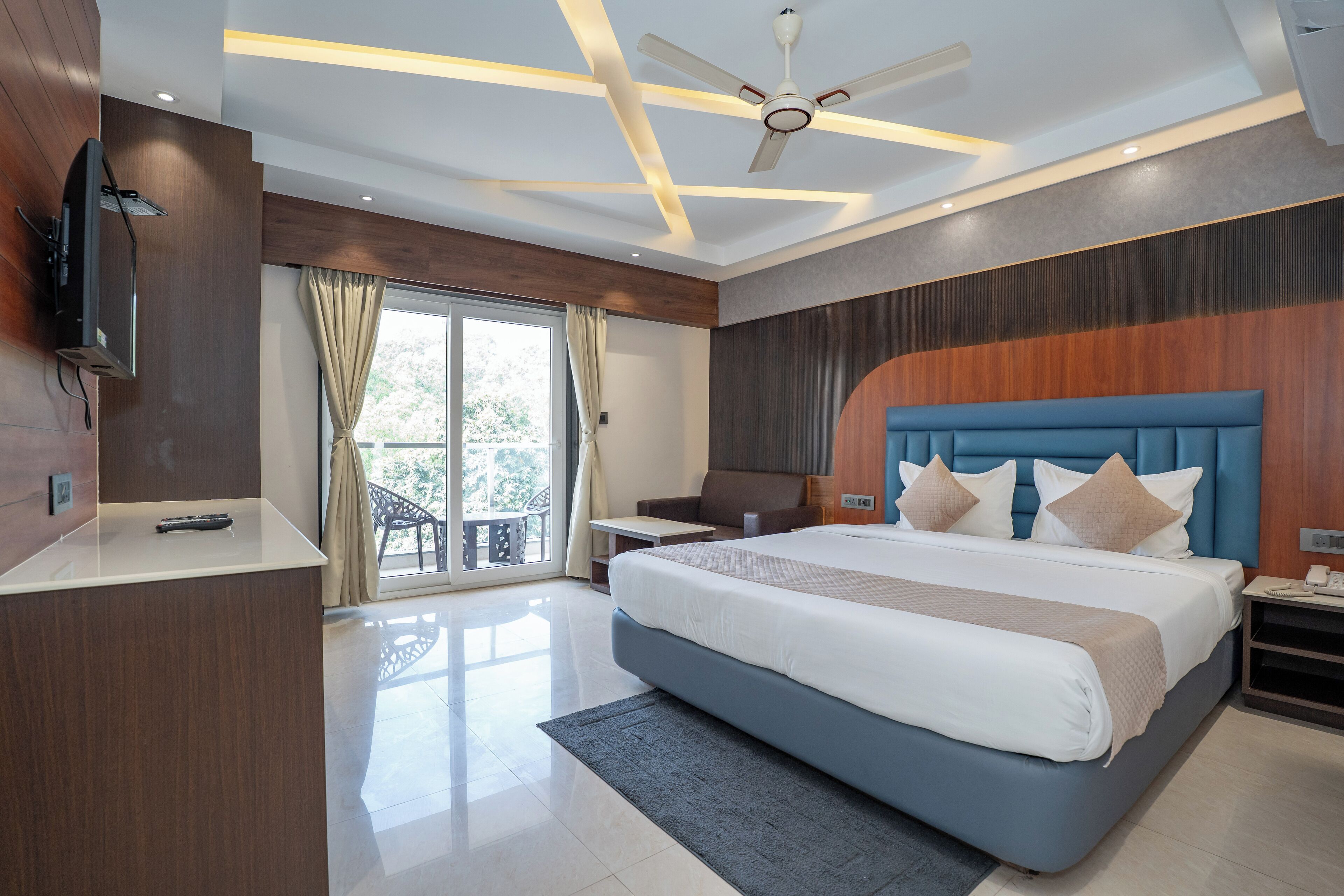 A modern bedroom with a large bed, a ceiling fan, and a TV mounted on the wall.