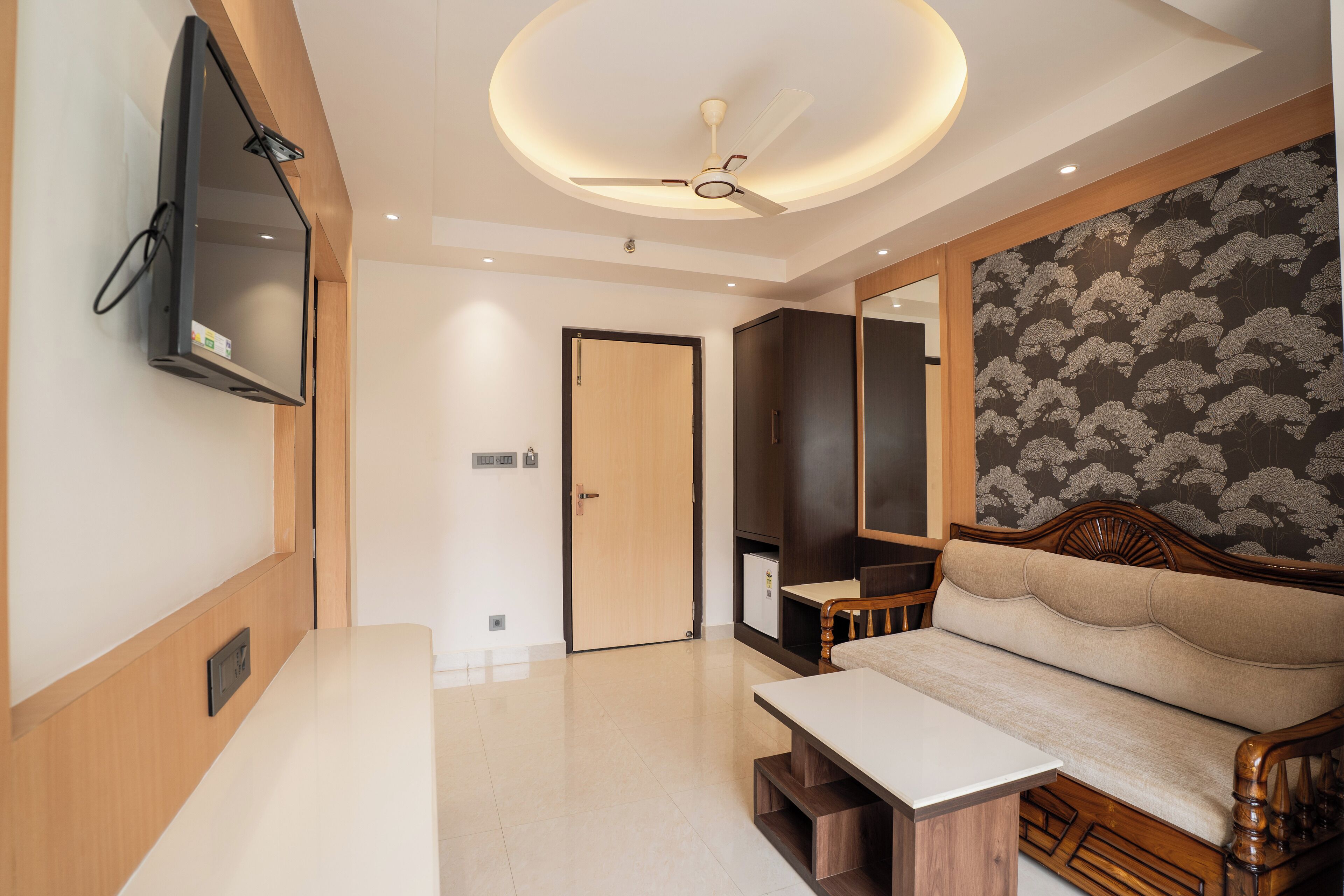 Un salon moderne avec un canapé, un téléviseur à écran plat fixé au mur, un ventilateur de plafond et une porte en bois.