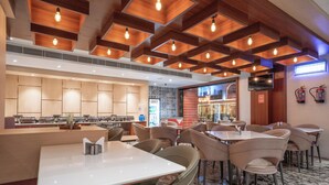 Een modern restaurant met een lange balie, verschillende zithoeken en een houten plafond met zichtbare balken en hangende lampen.