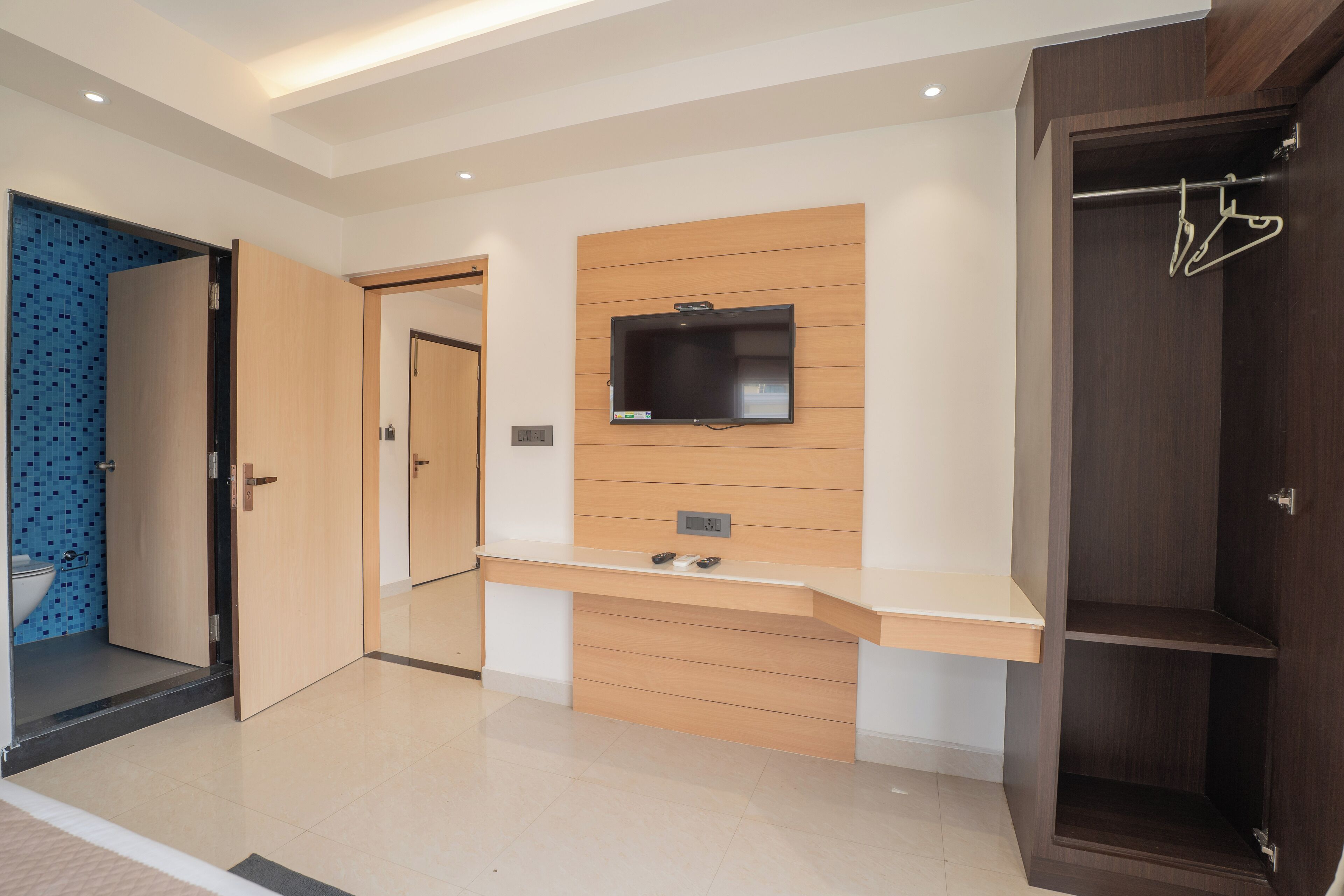 A modern bathroom with a wooden vanity, a mounted TV, and a walk-in closet with a hanging rack.