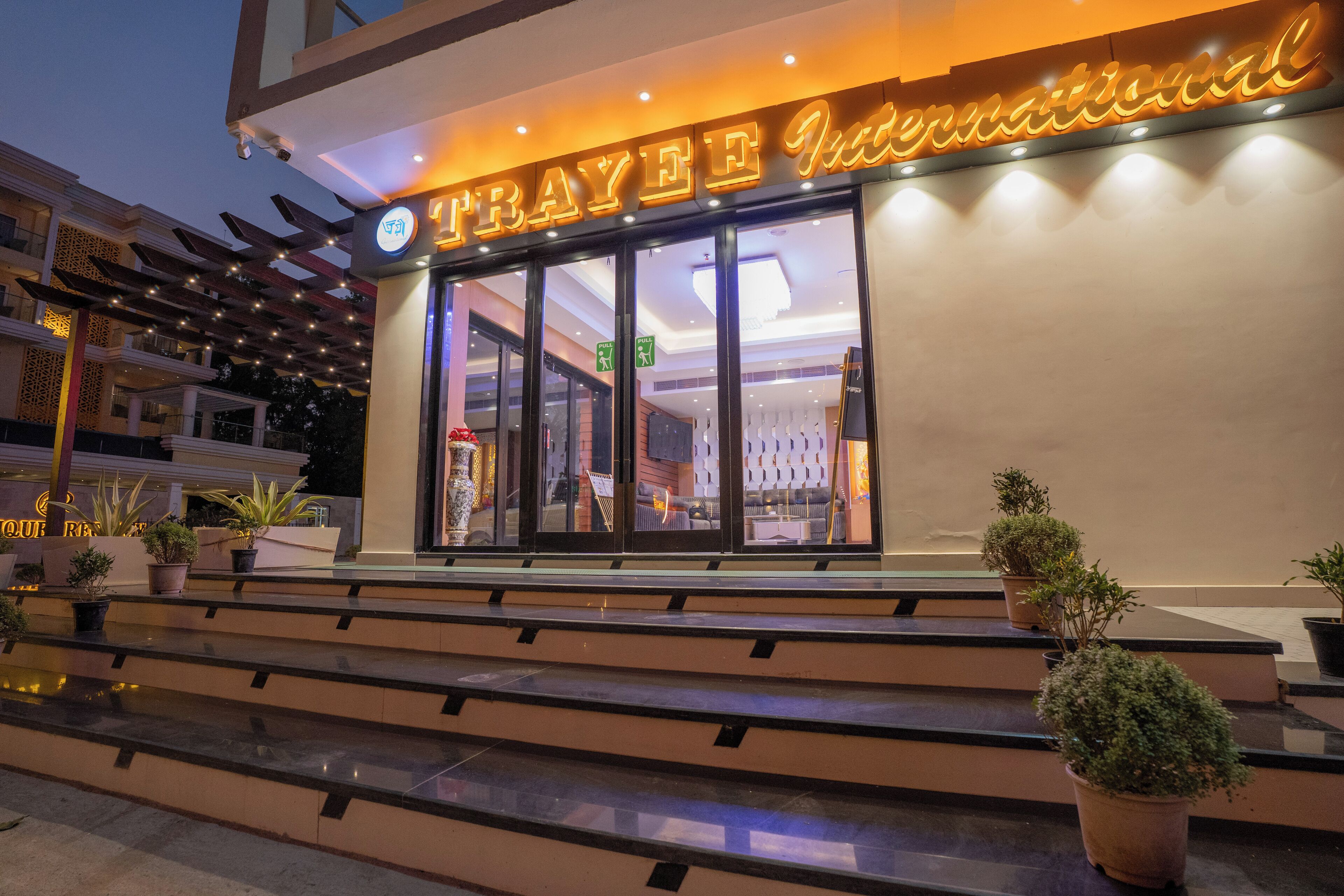 The exterior of a hotel named 'TRAYEEF International' with a modern facade, large glass windows, and potted plants on the steps.