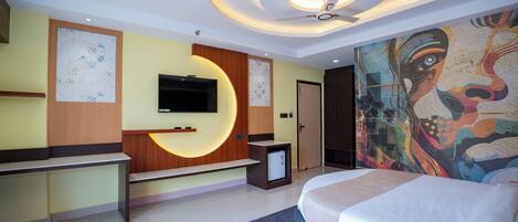 Una habitación de hotel moderna con cama, televisor, escritorio y un mural en la pared.