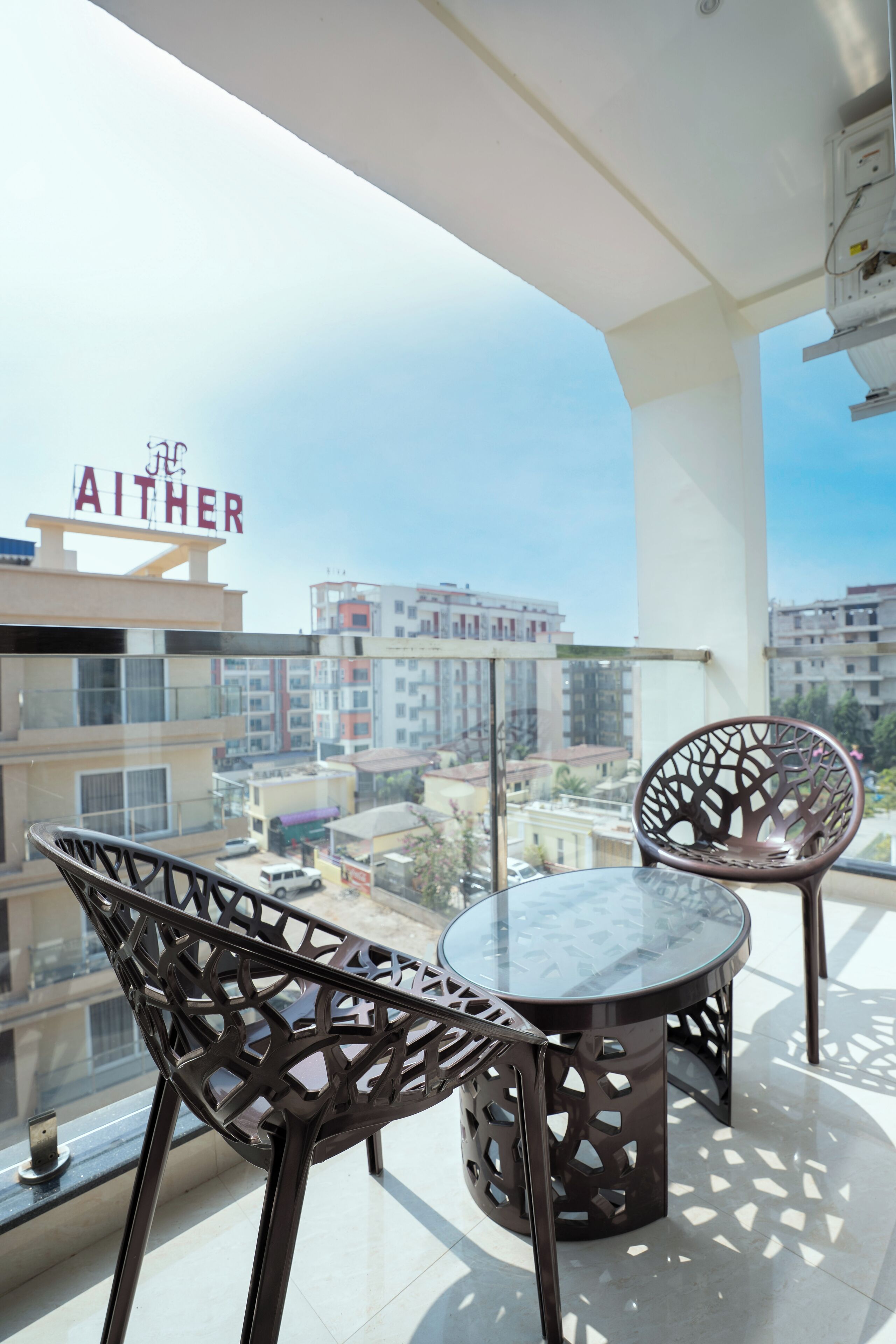 A balcony with two chairs and a table, overlooking a cityscape with buildings and a sign reading "AITHER".