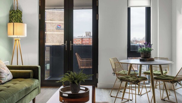 A modern living room with a green sofa, a round table with chairs, a floor lamp, and a view through a glass door to the outside. - York Retreat • Shambles • Free Parking • Gym Access (York)