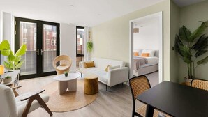 A modern living room with a white sofa, a round coffee table, and a dining table with chairs. There is a large window with blinds, a potted plant, and a view of a building outside. - City Gate York • Gym • Parking • Walk to Minster (York)