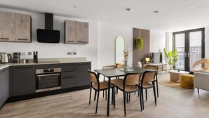 A modern kitchen with dark cabinetry, a built-in oven, and a coffee machine. There is a dining area with a round table and four chairs. - City Gate York • Gym • Parking • Walk to Minster (York)