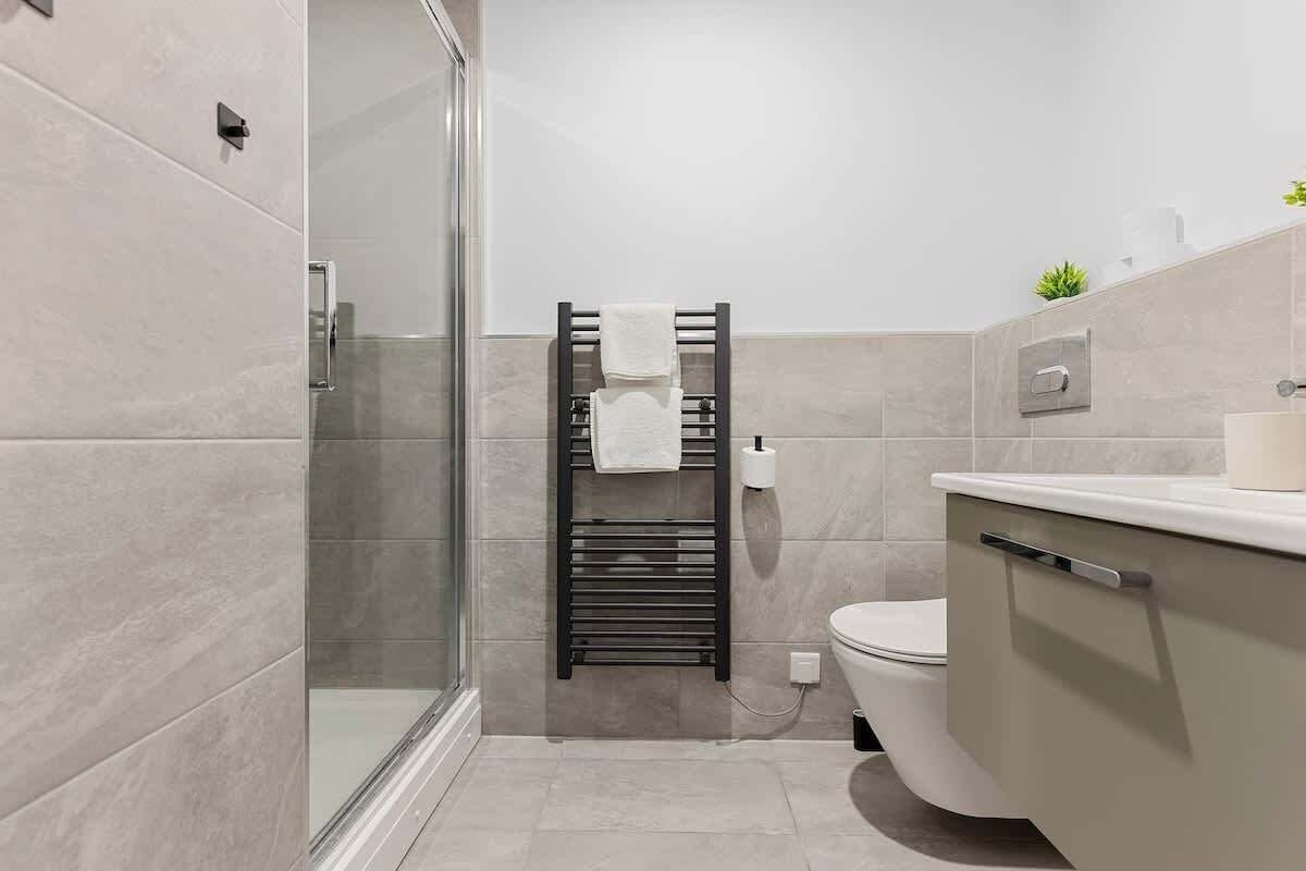 Une salle de bain moderne avec une douche à parois de verre, un porte-serviettes noir, des toilettes et un lavabo blanc.